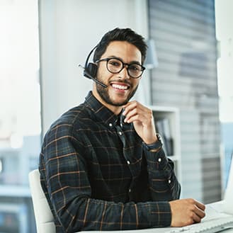 Your calls are answered in under 60 seconds by a human, not a machine. A smiling customer service representative seated at a desk wearing a telephone headset.