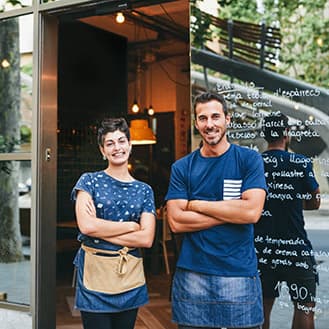 Couple of smiling storefront workers at main store door.