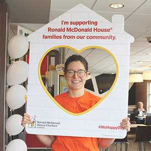 A smiling Pay it Forward volunteer posing behind an RMHC novelty photo frame.