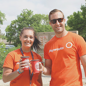 Pay it Forward - Tims Camps Two smiling Payworks Pay it Forward volunteers standing outside Tim Horton's location while holding Tim Horton's Coffee