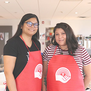 Pay it Forward - UnitedWay Two smiling Pay it forward volunteers standing side-by-side wearing UnitedWay aprons.