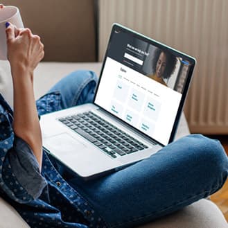 We Love Year-end. You read that right. Image of a person sipping a cup of coffee while sitting cross-legged looking at a laptop in their lap.